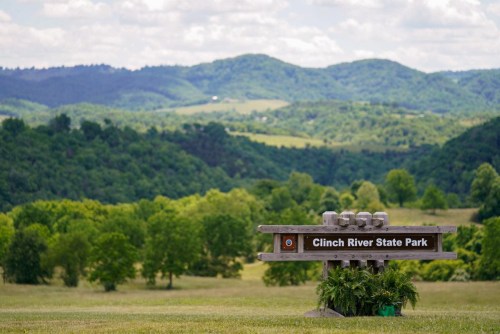 Sign for Clinch River State Park in front of lush green hills and a blue sky with scattered clouds.