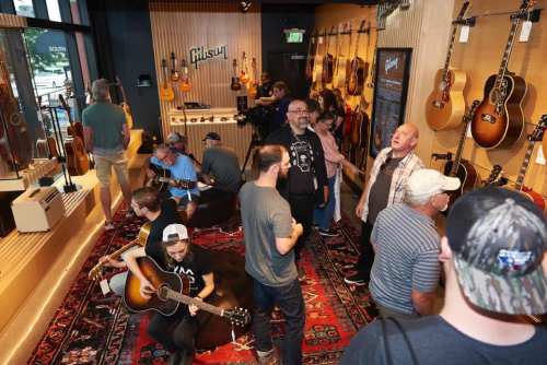 A lively guitar shop with people playing instruments and browsing, surrounded by various guitars on display.