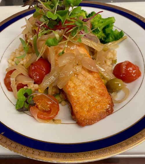 A beautifully plated salmon fillet with sautéed vegetables, cherry tomatoes, and microgreens on a decorative plate.