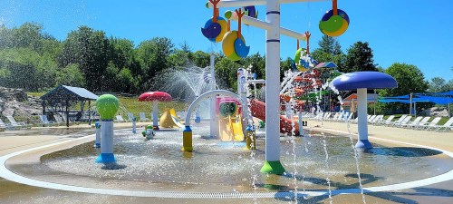 Colorful water play area with fountains, slides, and mushroom structures under a clear blue sky.