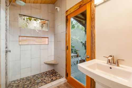 Modern bathroom featuring a walk-in shower, stone bench, and a wooden door leading to an outdoor area.