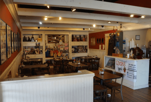 Interior of a cozy restaurant with wooden tables, shelves displaying memorabilia, and a counter at the front.