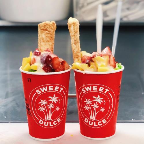Two red cups filled with colorful fruit, cream, and topped with crispy sticks, labeled "Sweet Dulce."