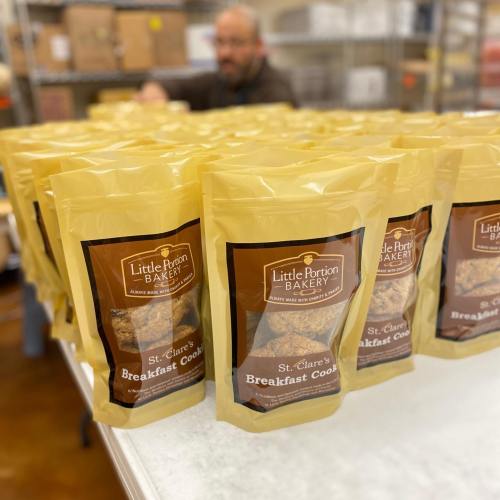 Bags of Little Portion Bakery's St. Clare's Breakfast Cookies arranged on a table, with a person in the background.