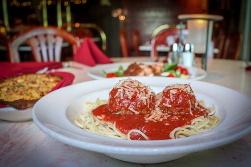 A plate of spaghetti topped with meatballs and marinara sauce, garnished with cheese, with other dishes in the background.