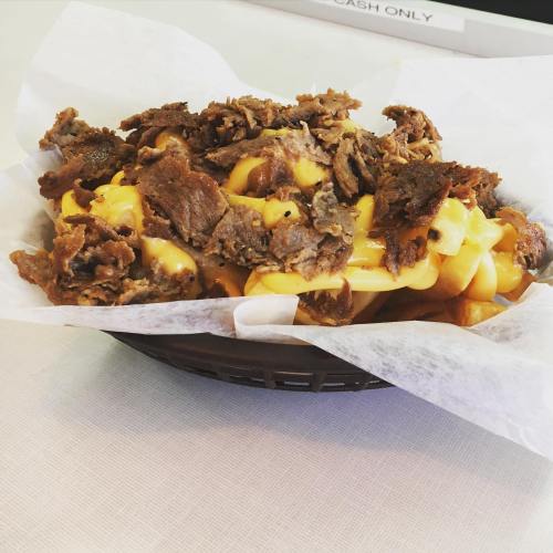 A basket of loaded fries topped with melted cheese and savory beef, served on a paper-lined plate.