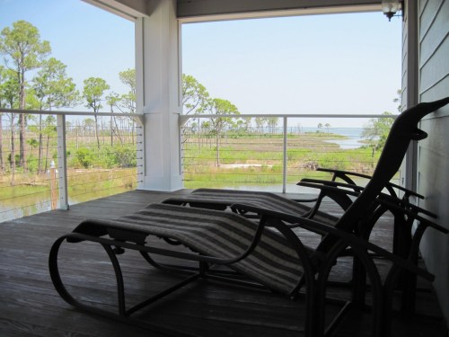 A serene balcony view with two lounge chairs overlooking a marsh and trees by the water.
