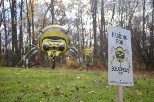 A large bee sculpture in a field with a sign reading "Parking for Schaefer's" in the foreground.