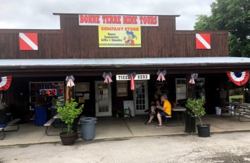 A rustic store with a sign reading "Bonne Terre Mine Tours," featuring outdoor seating and patriotic decorations.