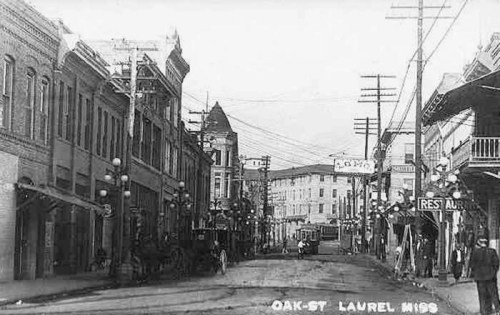 Historic black-and-white photo of Oak Street in Laurel, Mississippi, featuring buildings, streetcars, and power lines.