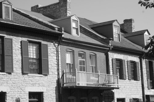 Historic stone building with a balcony, featuring multiple windows and shutters, in black and white.