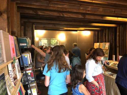 A busy bookstore interior with people browsing books and engaging in conversation. Shelves filled with various titles.