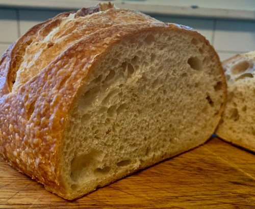 A close-up of a sliced loaf of bread, showcasing its golden crust and soft, airy interior on a wooden cutting board.
