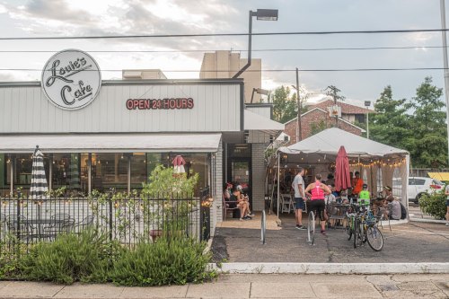 Exterior of Louis's Cafe with outdoor seating, a tent, and people enjoying the space. Open 24 hours.