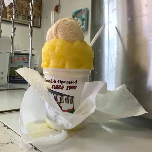 A colorful dessert cup with yellow slush and two scoops of ice cream, surrounded by napkins on a counter.
