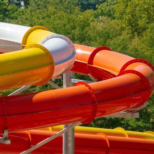 Colorful water slides twist and turn against a backdrop of green trees on a sunny day.