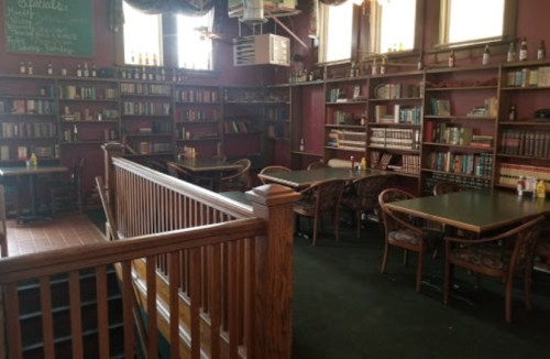 Cozy interior of a restaurant with bookshelves, tables, and chairs, featuring warm lighting and a welcoming atmosphere.