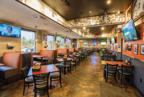 Interior of a sports bar with booths, tables, and multiple TVs displaying sports events. Brightly lit and inviting atmosphere.