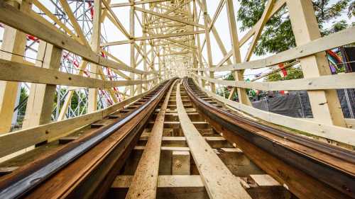 View from the tracks of a wooden roller coaster, curving upward through a wooden structure.