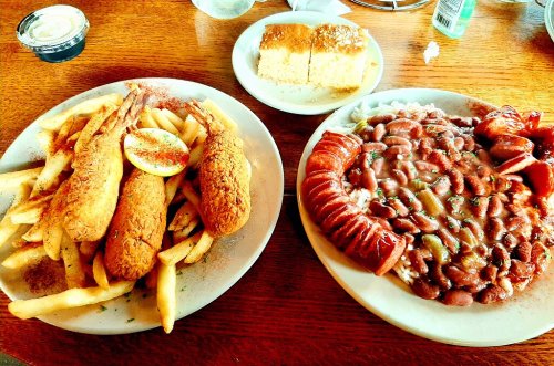 A plate of fried shrimp and fries, alongside a dish of beans and sausage, with a roll in the background.