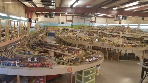 A large model train layout featuring intricate tracks, buildings, and landscapes in a spacious indoor setting.