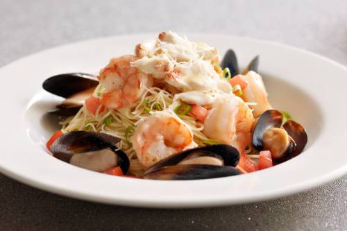 A plate of pasta topped with shrimp, crab, and mussels, garnished with diced tomatoes and green onions.