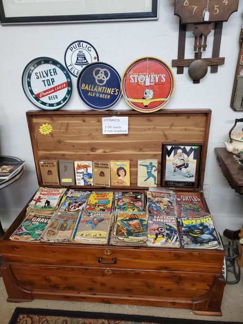 A wooden chest filled with vintage comics, surrounded by decorative beer signs on the wall.