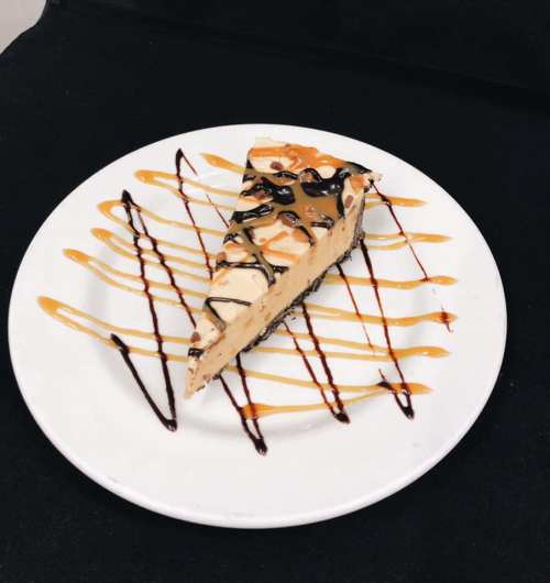 A slice of dessert on a white plate, drizzled with chocolate and caramel sauces.