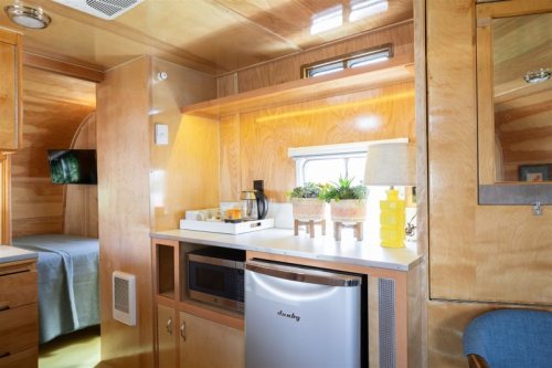 Cozy interior of a modern trailer, featuring a kitchenette with a fridge, coffee maker, and decorative plants.