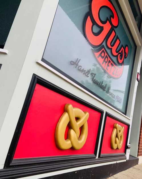 Close-up of a storefront window featuring the name "Gus' Pretzels" and decorative pretzel designs in gold and red.