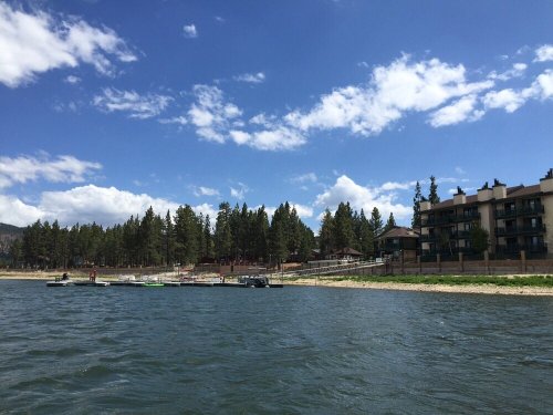 A serene lake scene with a dock, boats, and a forested shoreline under a blue sky with fluffy clouds.