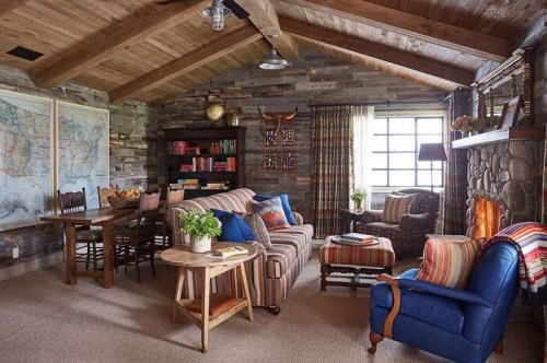 Cozy living room with wooden walls, a stone fireplace, striped furniture, and a large map on the wall.