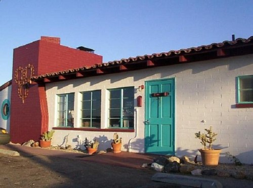 A colorful building with a red and white exterior, turquoise door, and potted plants in front.