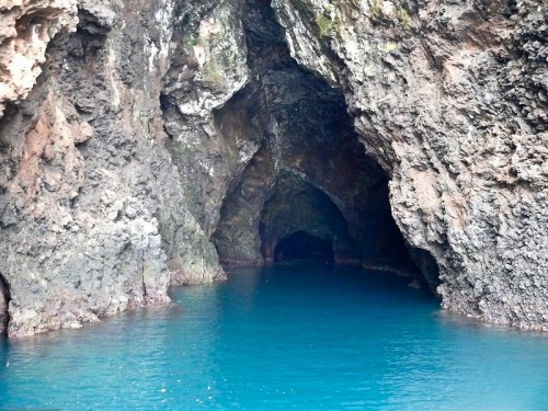 A serene cave entrance with dark rocky walls and calm turquoise water inside.