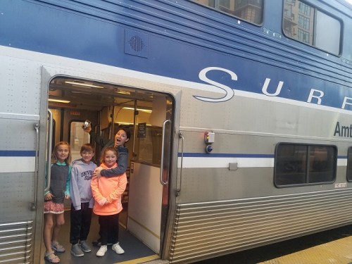 Four children stand at the open door of a train, smiling and posing for the camera.