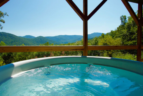 A hot tub on a deck with a scenic view of green mountains and a clear blue sky.