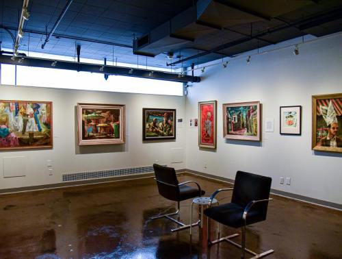 Art gallery interior featuring colorful paintings on the walls and two black chairs in the center.