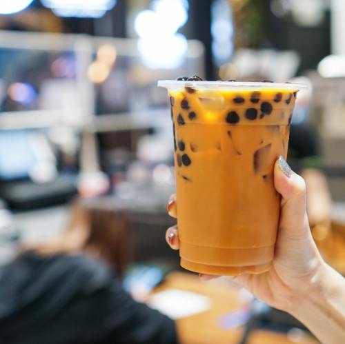 A hand holding a clear cup of iced bubble tea with brown tea and black tapioca pearls.