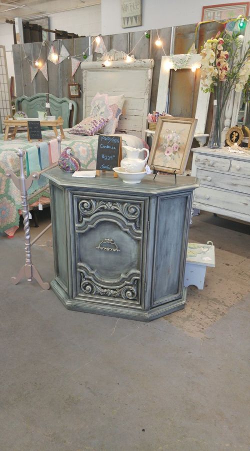 A vintage-style corner cabinet with ornate detailing, surrounded by decorative items in a charming shop setting.