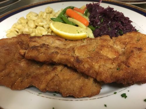 A plate of crispy fried schnitzel with lemon, macaroni, mixed vegetables, and red cabbage.