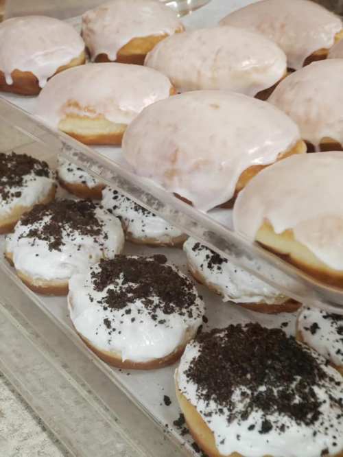 A display of glazed donuts, some topped with white icing and crushed cookies, arranged on a tray.