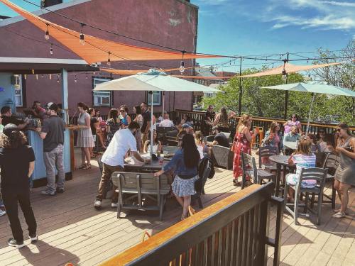 A lively rooftop gathering with people socializing, enjoying drinks, and sitting under umbrellas on a sunny day.