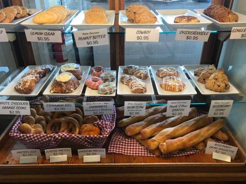 A display case filled with various baked goods, including cookies, pastries, and pretzels, with prices listed.
