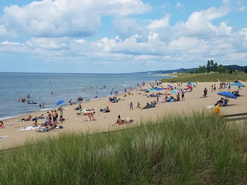 A sandy beach with people sunbathing, swimming, and colorful umbrellas under a partly cloudy sky.
