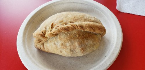 A golden-brown calzone on a paper plate, resting on a red table.