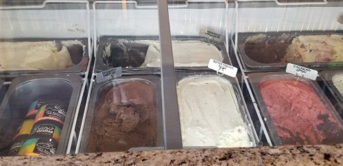 A display of various ice cream flavors in metal tubs, including chocolate, vanilla, and strawberry.