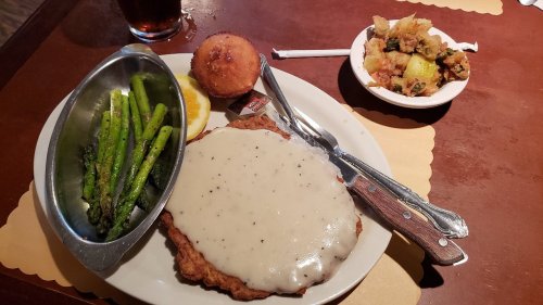 A plate with fried chicken topped with gravy, asparagus, a cornbread muffin, and a side of mixed vegetables.