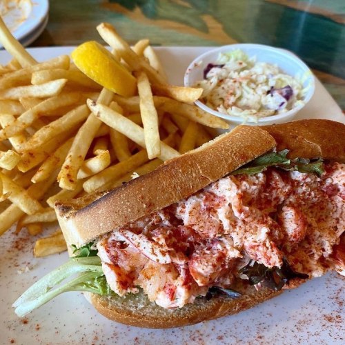 A lobster roll on a bun with lettuce, served with fries and a side of coleslaw, garnished with a lemon wedge.