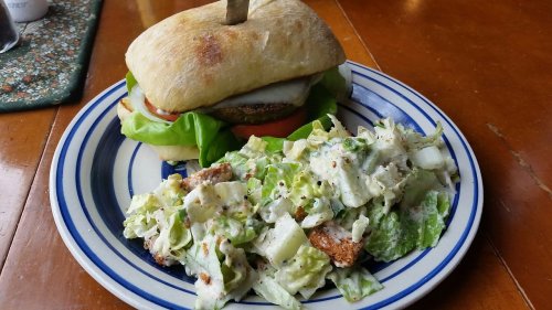 A sandwich with lettuce, tomato, and a patty, served with a side of Caesar salad on a blue-striped plate.