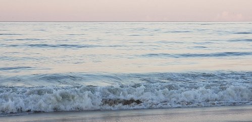 Calm ocean waves gently lapping at a sandy shore during a serene sunset.